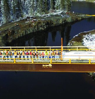A group of workers gather on a bridge celebrating the successful construction of Peter Sutherland Sr. hydroelectric station.