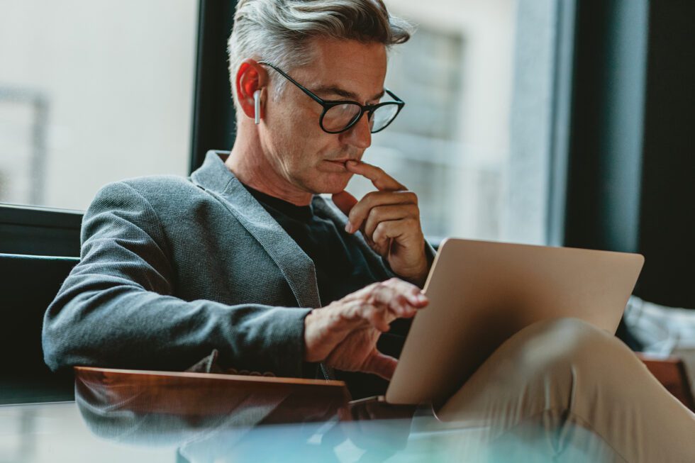 Businessman looking at laptop and thinking. Businessman reading emails on laptop in office lobby.
