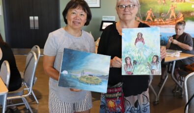 Two visitors hold up their paintings during the Indigenous Creations event at OPG's Saunders Hydro Dam Visitor Centre.