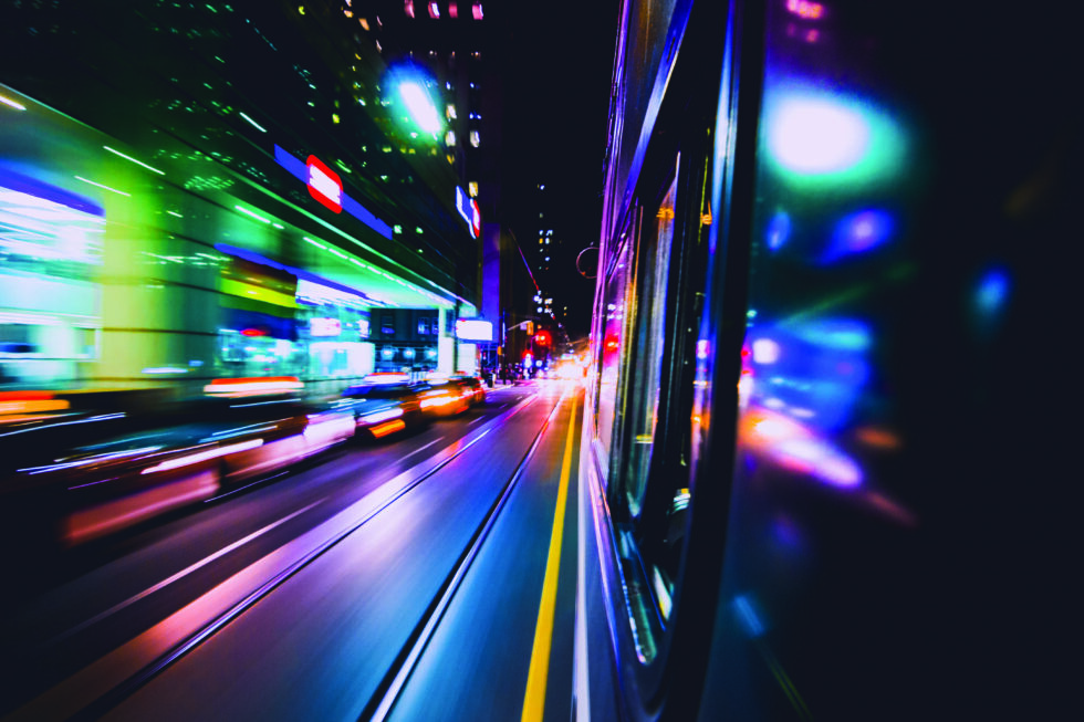 Fast-motion public transit vehicle speeding down street core with beautiful color streaks. Train transportation.