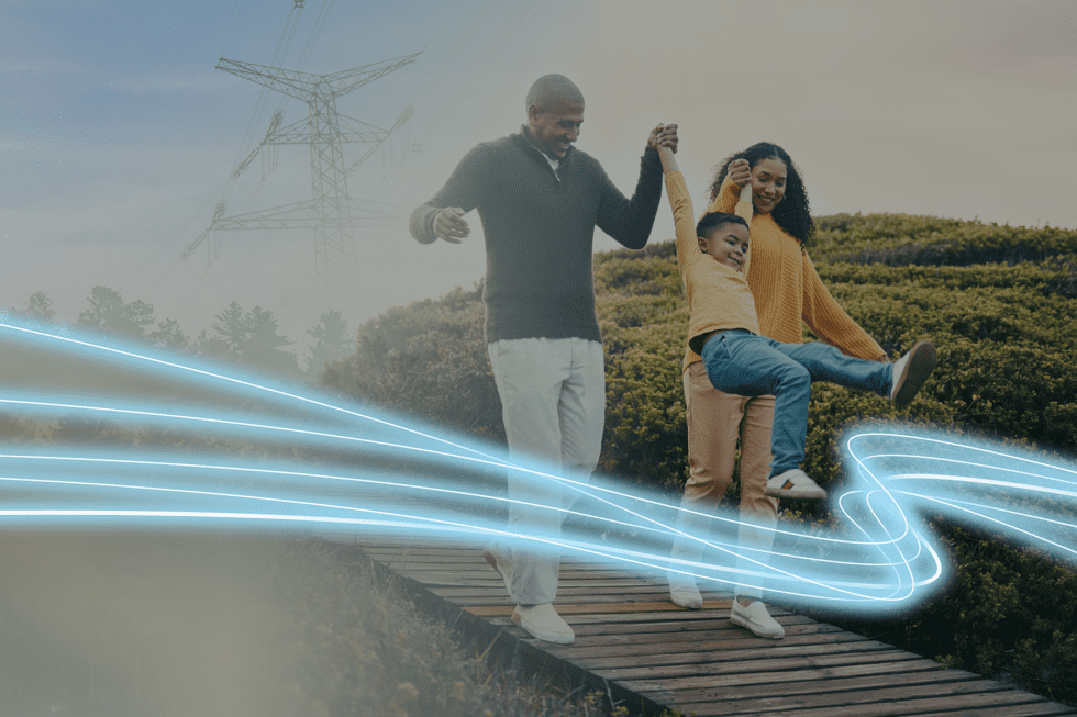 A family of three walk along a boardwalk with power transmission lines in the background.
